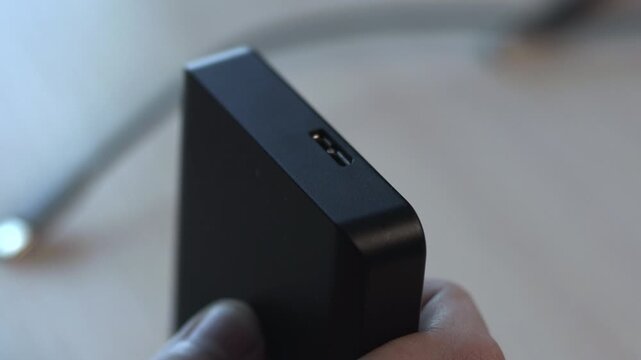 Attaching Charger To Black Hub. Closeup Of Hands Linking Power Cord To Compact Charger On Desk Surface. Media