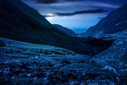 road through mountains winding uphill at night. full moon over popular highway travel destination of Romania. mysterious view of mountain on summertime weather. road journey landscape