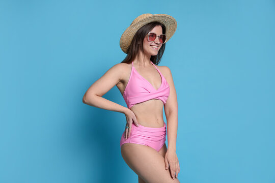 Woman in pink swimsuit, hat and sunglasses on light blue background
