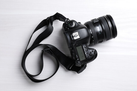 Modern camera with strap on white wooden table, top view