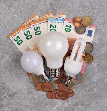 Cost of electricity concept, lightbulbs and money on a gray stone background