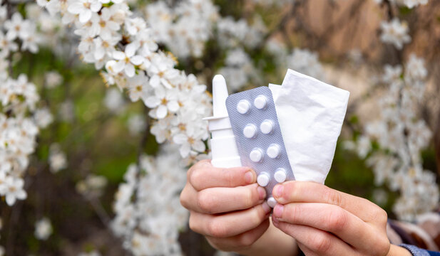 Child holding nasal spray, pills and tissue against a blooming tree. Allergy