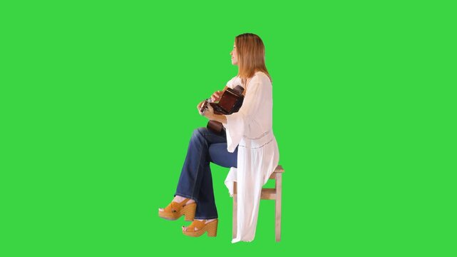 Nice caucasian girl in white dress plays acoustic guitar on a Green Screen, Chroma Key.