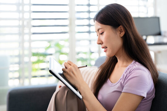 Young Asian woman studying online, sitting on sofa with teblet at home.