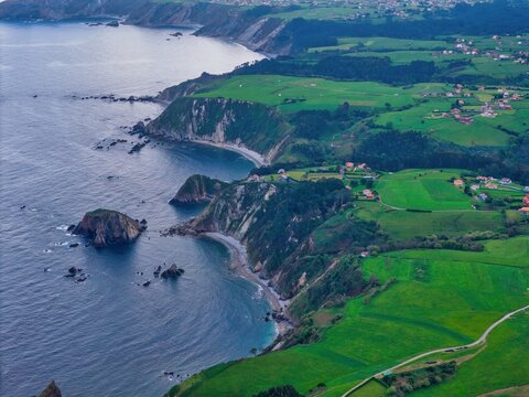 Aerial view of the rugged coastline of Silence Beach Viewpoint with steep cliffs and lush green fields in Cudillero, Asturias, Spain.