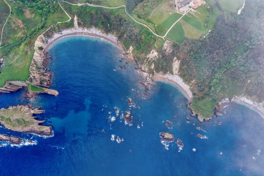 Aerial view of Silence Beach Viewpoint with its crescent-shaped bay, turquoise waters, and dramatic rocky cliffs surrounded by lush green hills Cudillero, Asturias, Spain.
