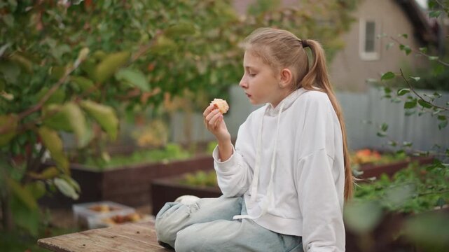 Caucasian girl sitting on bench munching apple in suburban garden, wearing hoodie and jeans with ponytail, warm autumn light and soft bokeh, contemplative expression, amateur gardener daydream, rustic