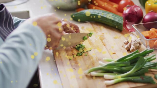 Cook placing herbs, chopping on board with knife, forming pile for prep, yellow-bokeh over hands