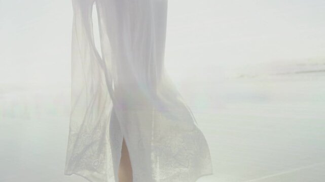 Mid-adult woman walking stepping onto wet sand causing light glow accenting dress slit for fashion