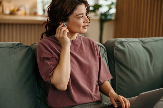 Woman wearing wireless earbuds using laptop working from home
