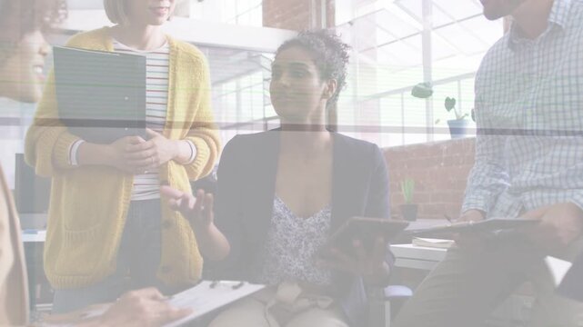 Seated woman tapping tablet and leading meeting in office, spawning animated charts showing sales