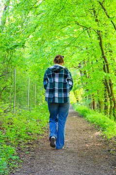 Woman walking down a sun-dappled forest path surrounded by vibrant green foliage