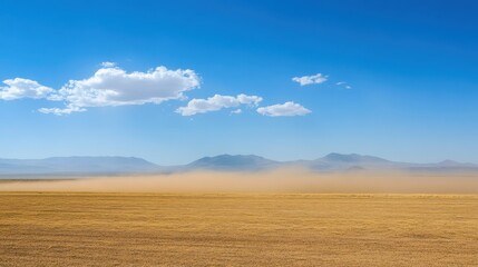 Fototapeta premium Dust storm obscuring distant mountains across a dry desert landscape under a blue sky with scattered clouds