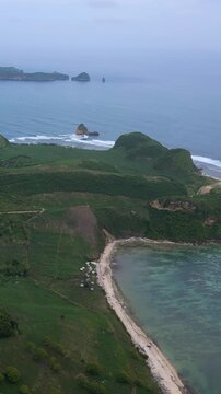 Aerial Green Island Cape With Curved Beaches, Rolling Hills And Farmland Pockets, Long Reef Line Shaping Waves, Secluded Bays, Turquoise Shallow Water Meeting Deep Ocean, Katil beach,Lombok,Indonesia