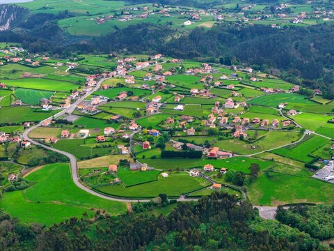 Aerial view of a rural village with houses scattered among lush green meadows and winding roads in Cudillero, Asturias, Spain.