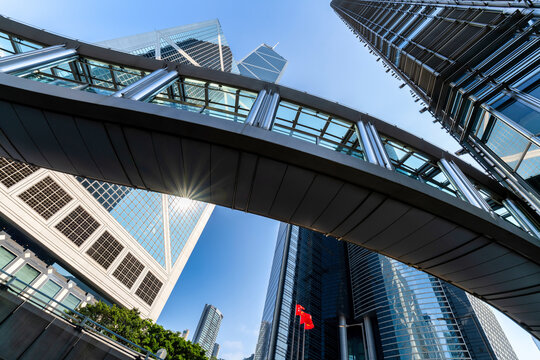 Looking up at the iconic Bank of China Tower and modern skyscrapers under a clear blue sky in Central, Hong Kong during a bright afternoon.