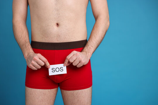 Urology. Man in red underwear holding note with word SOS on light blue background, closeup. Space for text