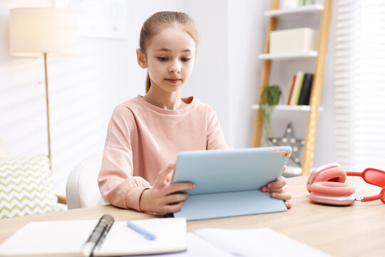 Cute girl with tablet doing homework at table indoors