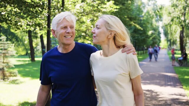 Smiling senior couple enjoys a walk through a sunny green park, spending quality time together and embracing active, joyful aging.