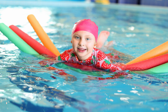 Cute little girl swimming with water noodles during lesson in pool