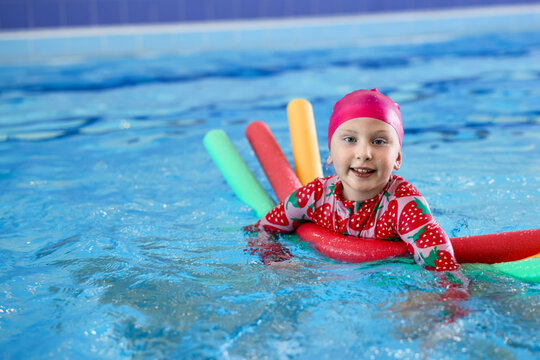 Cute little girl swimming with water noodles during lesson in pool, space for text