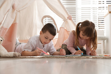 Little kids drawing in sketchbook together near toy wigwam at home © New Africa
