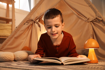 Little boy reading book near toy wigwam at home © New Africa