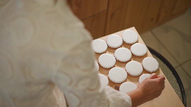 Baker arranging pumpkin pie tartlets on tray near wooden counter, closeup of hands in lace sleeve placing round pastries into liners, warm autumn lighting with powdered sugar dusting, ready for sale