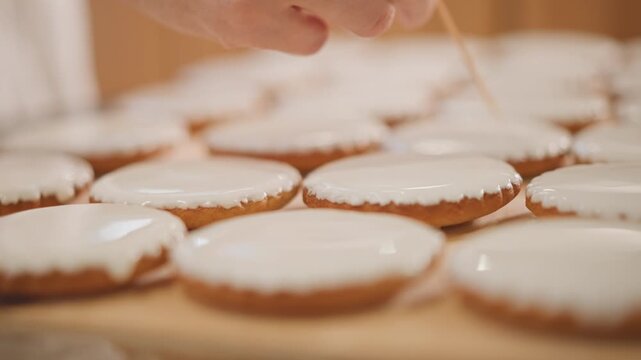 Closeup hand detailing icing on pumpkin cookie, toothpick smoothing glaze, shallow focus, warm brown crust edges, glossy surface, slow precise motion, studio light, satisfying food shot