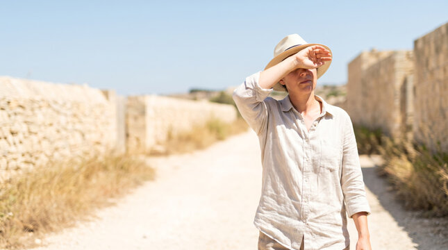 mature man shielding eyes from sun while walking in arid desert landscape during golden hour
