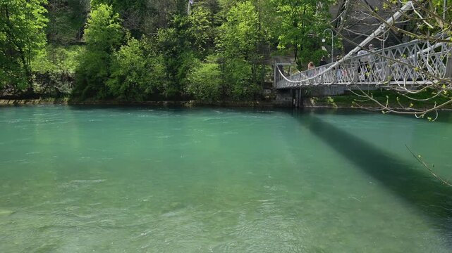 Clear turquoise river flowing past lush green trees on a sunny spring day near Morges, Switzerland.