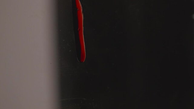 Blood Drops of Red Liquid Slowly Dripping Down a Dark Surface Against a Black Background
