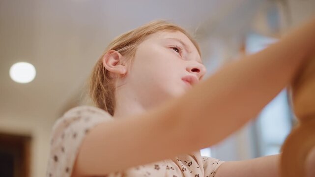 Young white girl reaching for pie dish, low angle closeup of determined expression as she stretches across countertop in warm kitchen light, apron on, focused hands handling baking tray, candid