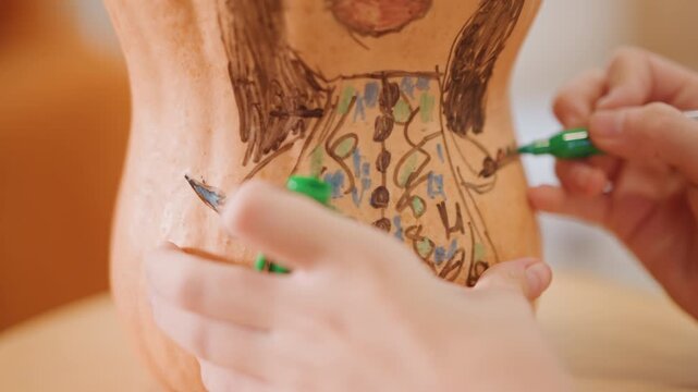Closeup pumpkin pattern colored with green marker. Focused hands fill intricate dress motif on gourd, green marker accents, repeat lines and dots, close tabletop view, calm workshop mood, seasonal