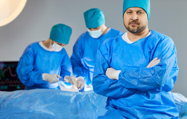 Fototapeta premium Surgeon confident man, group professional medical doctors surgical team performing surgery, doing operation, procedure on patient, wearing blue surgical gown, cap, face mask, treat injuries, diseases
