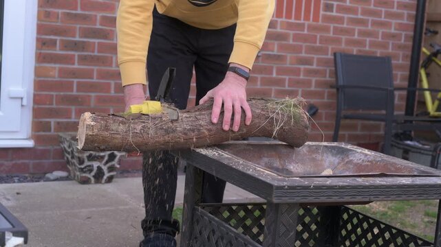 Man Cutting a Thick Log with a Cordless Mini Chainsaw in Garden
