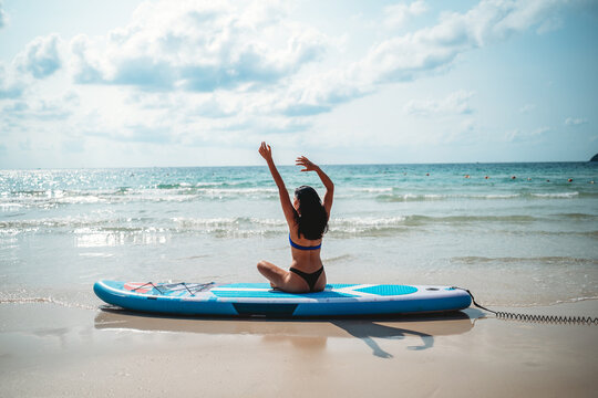Meditating woman in lotus pose on a paddle board on a tropical beach on summer vacation