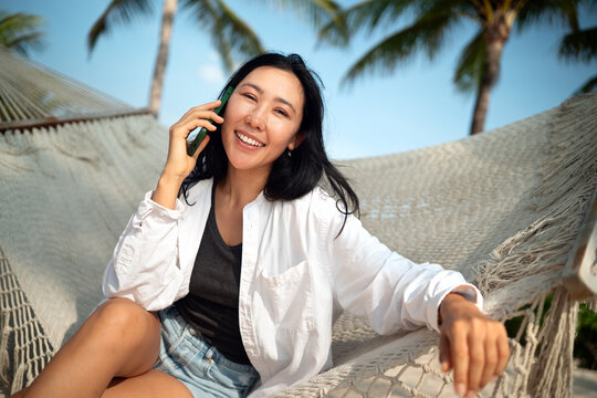 Cheerful woman talking on a smartphone during a sunny day at a tropical beach on summer vacation