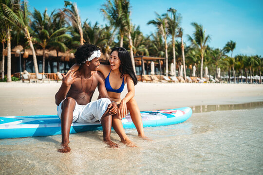 Young multiethnic people, couple having fun on surfboards in the clear ocean water during summer