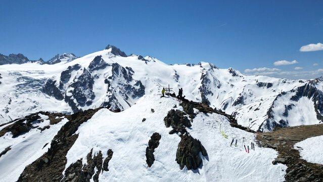 Aerial view of Pointe Ronde summit with skiers and a summit cross overlooking snow-covered peaks and rocky ridges under a clear blue sky in Trient, Valais, Switzerland.