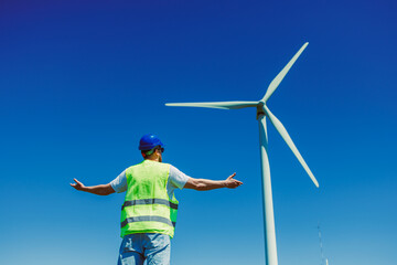 Windmill engineer stands near turbine under clear blue sky during daytime at wind farm site © DSMT