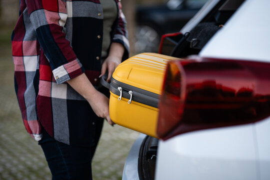 Person loading yellow suitcase into car trunk for road trip
