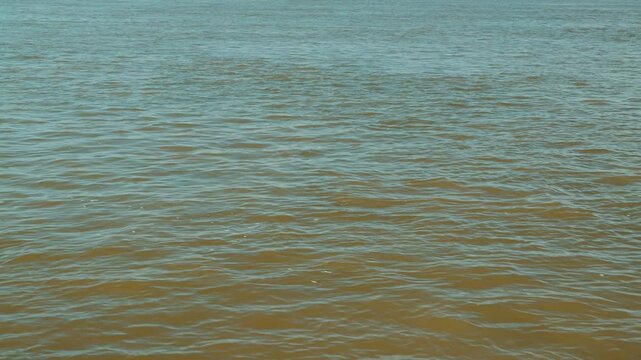 Minimalist view of murky brown river water with gentle ripples creating natural abstract texture. Calm, serene background for concepts of nature, environment, tranquility