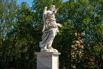 Fototapeta premium Marble angel statue on Ponte Sant Angelo bridge in Rome Italy isolated against green trees background with clear daylight