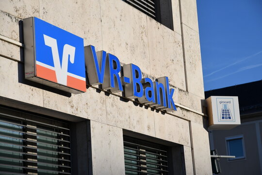 Close-up view of a VR-Bank logo and signage mounted on a building exterior, with a nearby &ldquo;girocard&rdquo; ATM sign visible