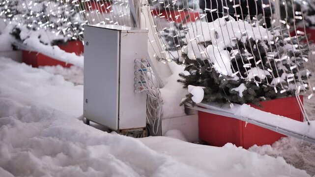 City sidewalk with snow, Christmas lights, white electrical box, and seasonal decoration