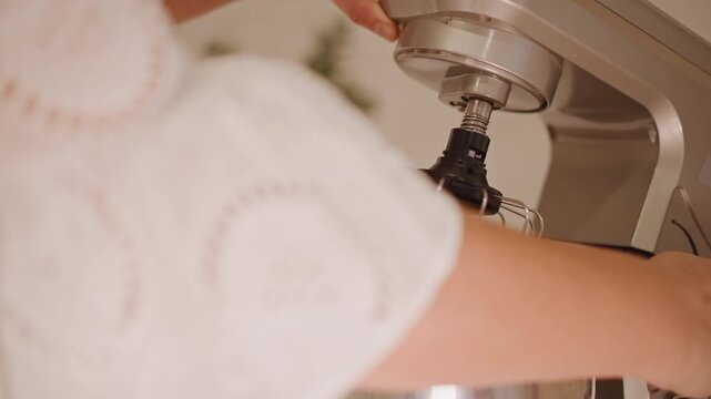 Hands attaching mixer whisk to bowl cozy kitchen home baker assembling stand mixer attachment for pumpkin pie filling closeup shots of stainless steel bowl whisk hands warm natural light blurred