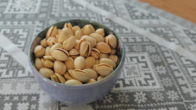 A detailed close-up of a rustic ceramic bowl generously filled with roasted and salted pistachios, placed on a beautifully patterned tablecloth, highlighting this nutritious and tasty snack option.