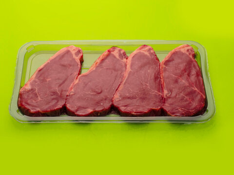 Tray with four strip loins in a vacuum pack plastic tray for exceptional freshness. Fine high value and quality beef meat. Green color background.