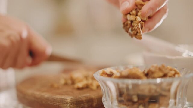 Closeup hands transferring chopped walnuts into bowl, gentle scoop into glass dish, knife resting on board, warm light and seasonal mood, preparing pie topping for Thanksgiving dessert